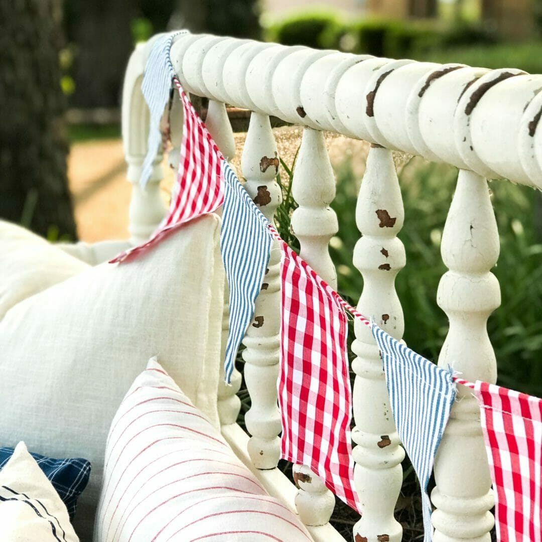 White chippy bench with red, white and blue flag garland draped on back with pillows