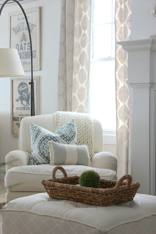 white chair in front of window with curtains, lamp and basket on ottoman