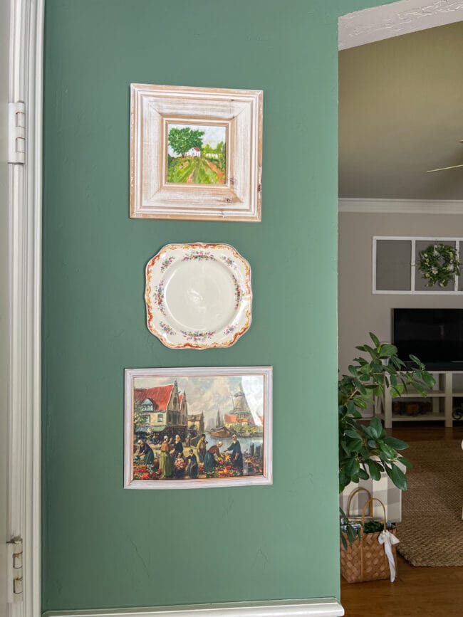 2 paintings with a small square plate hanging on a green wall 