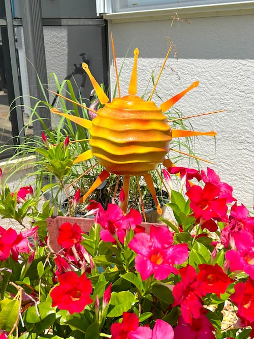 yellow DIY sun sitting in a garden with red flowers