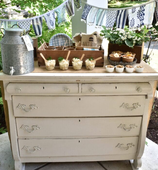 vintage dresser in cream, blue and white banner across the back with galvanized drink jug, paper and plastic goods 