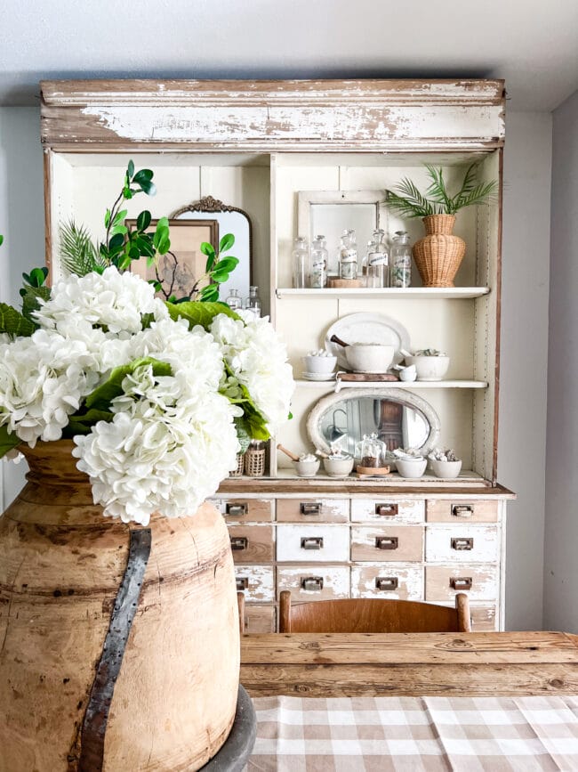 white hutch with large jar of hydrangeas on table