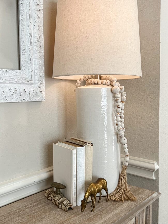 white lamp with beads, white books and a brass horse with an old cabinet latch