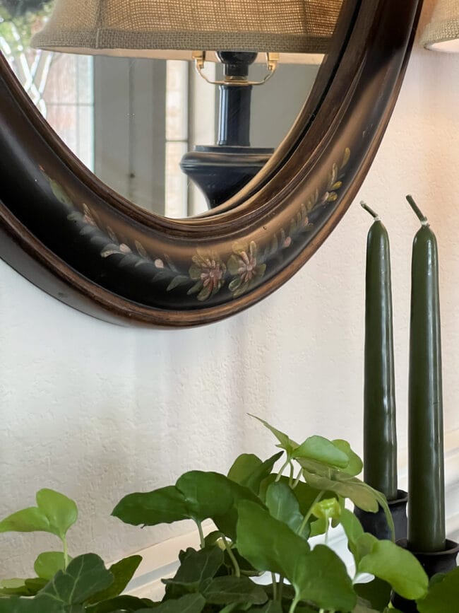 close up of edge of black oval mirror, plant and green tapered candles