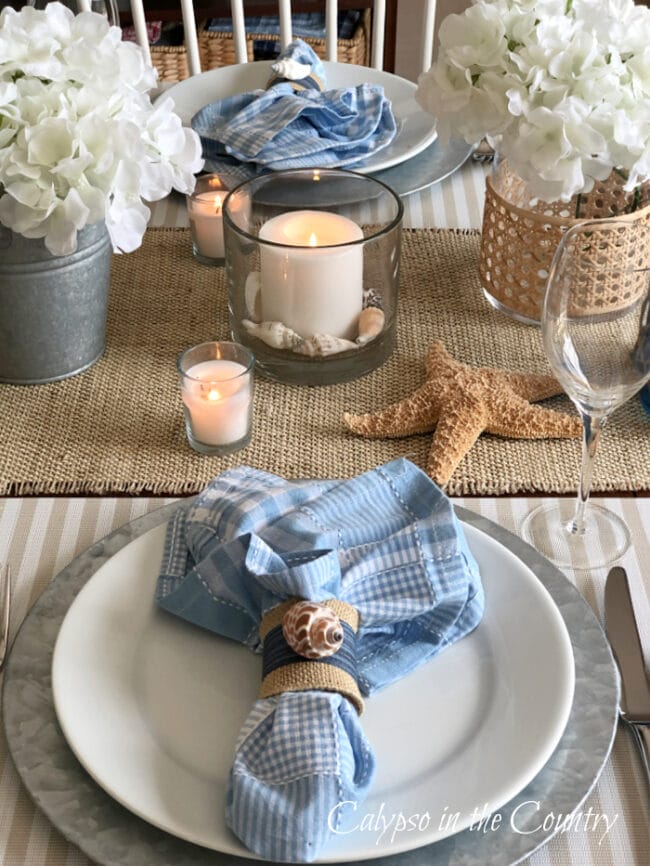 table scape with white plates, blue napkins, starfish and candles