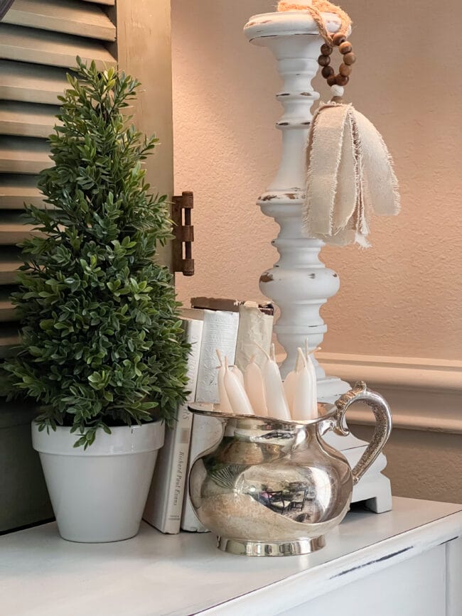 close up of cone shaped topiary, books, lamp and white candles inside a silver pot