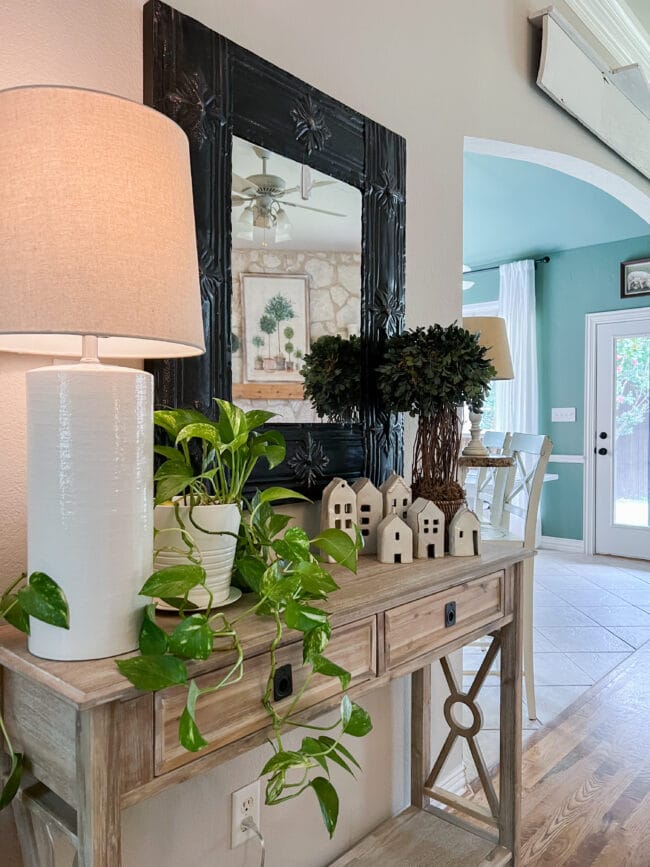 console table with white lamp, plant, black mirror and house collection