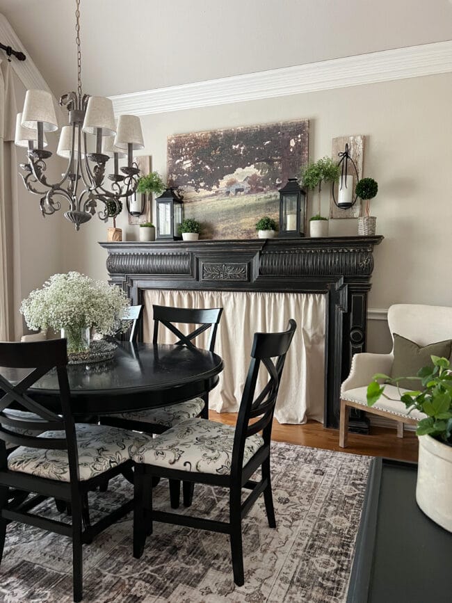 dining room with black table, mantel with topiaries and lanterns