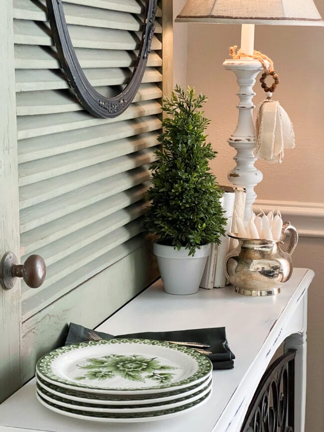 close up of green stacked plates, lamp, topiary and silver pot with white candles