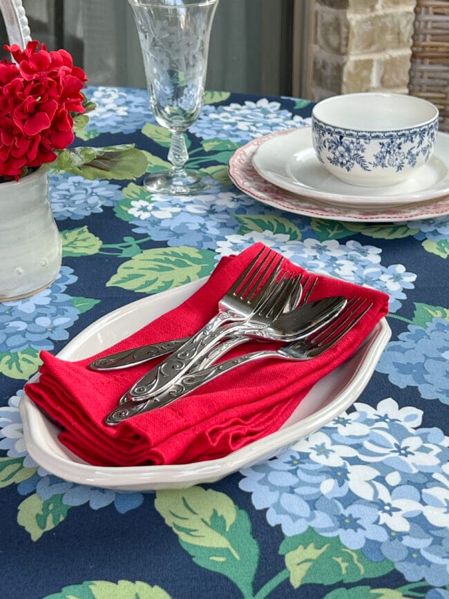 blue and green hydrangea tablecloth with a platter of red napkins and flatware