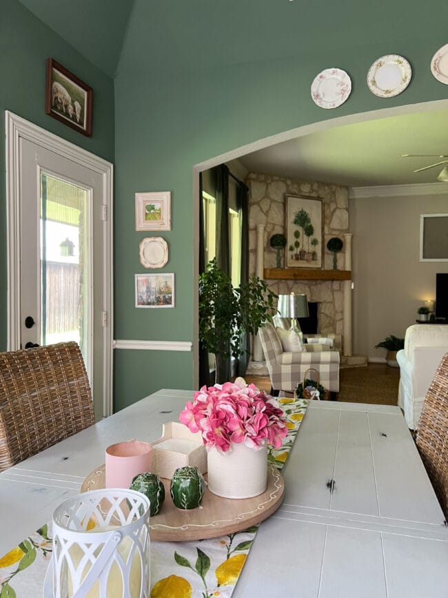 green walls with plates and prints. white kitchen table with pink flowers