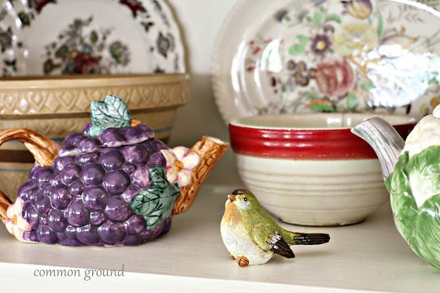 grape teapot, small bird, old bowls and vintage floral platters on a shelf