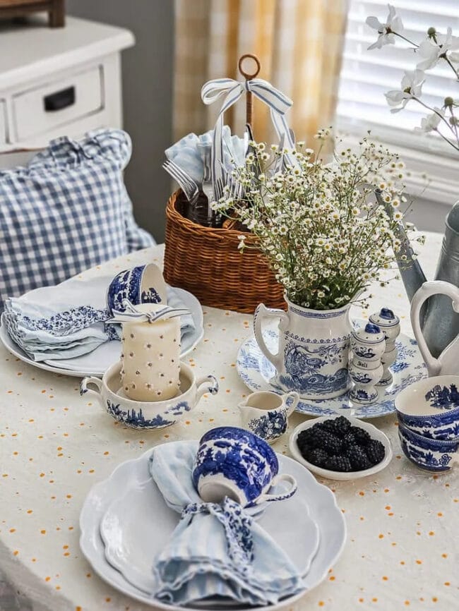 blue and white tablescape with vintage dishes, pillows and flowers