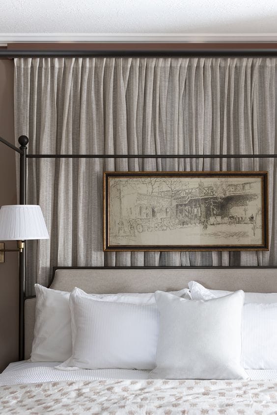 wall of taupe curtains behind an iron bed with a painting over headboard