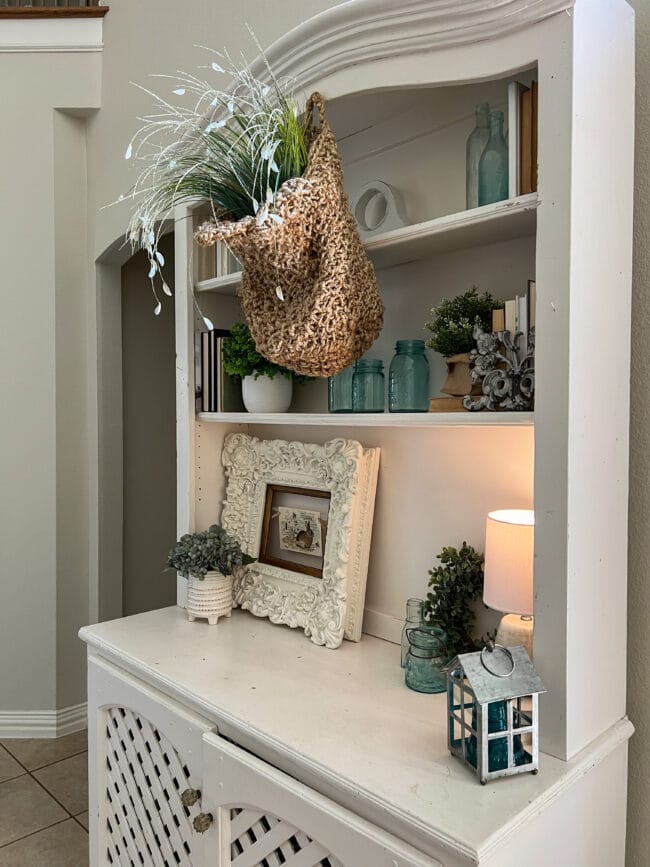 white hutch with hanging basket of spring stems, white frame with bunny and lots of blue bottles and smaller greenery plants