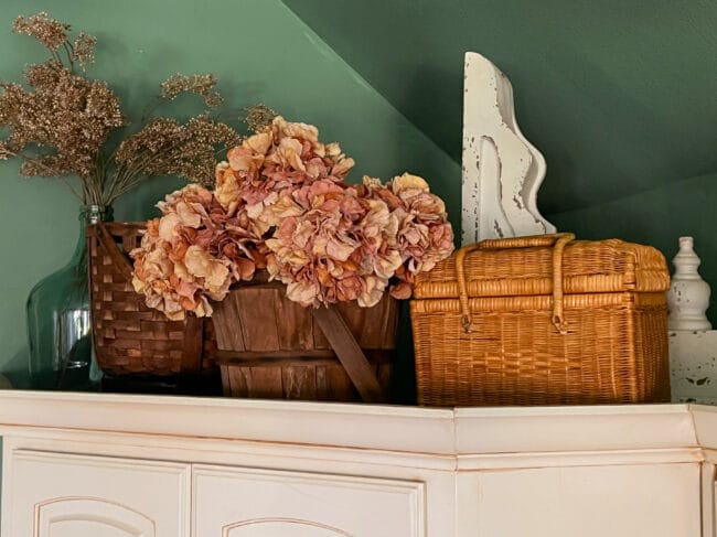 3 vintage baskets and flowers on upper kitchen cabinets with green walls