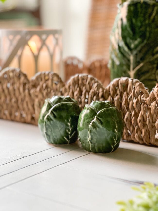 close up photo of green cabbage salt and pepper shakers sittin in front of a woven basket tray