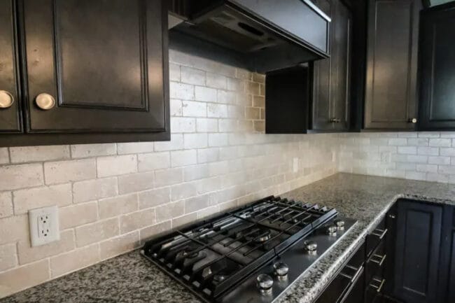 dark cabinets with stove top and painted backsplash