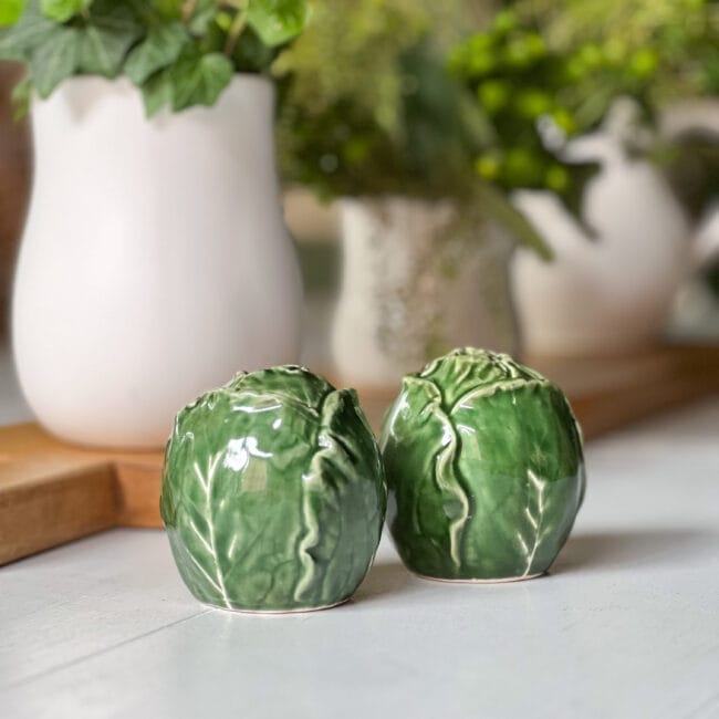 Green cabbage salt and pepper shakers with white vases and plants inside on a table