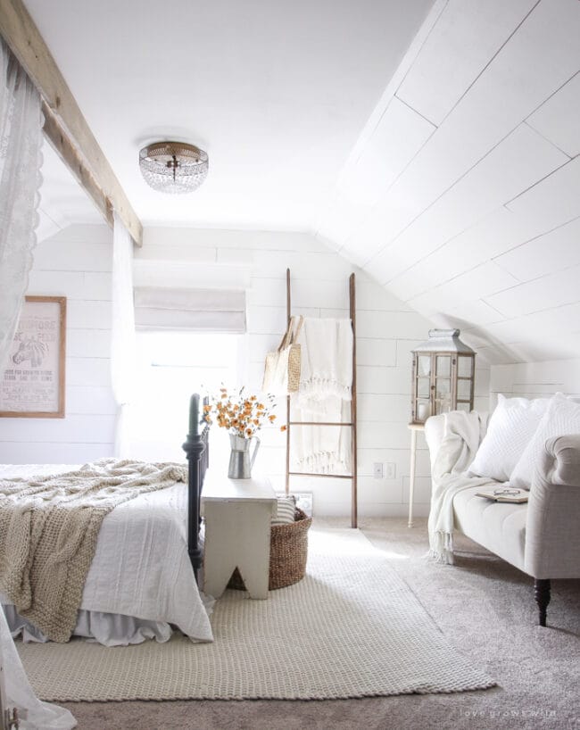 white farmhouse bedroom with ladder next to window and loveseat on right with bed on left of room