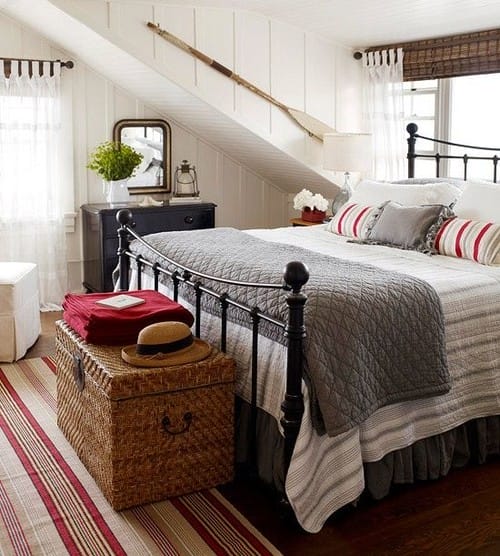 black iron bed with chest at end, striped bedding and an oar angled on the wall