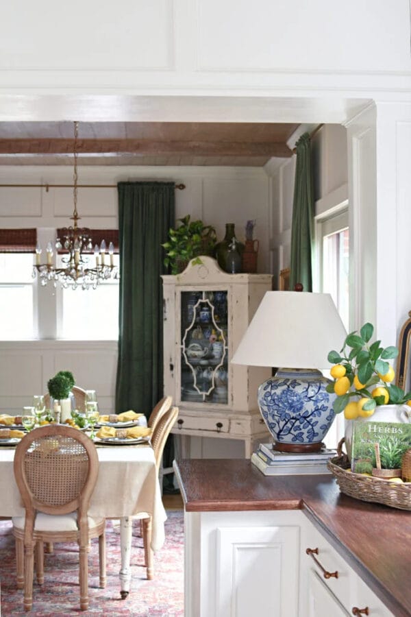 dining room with white hutch in corner, lamp on table, green curtains and a lemon themed dining table