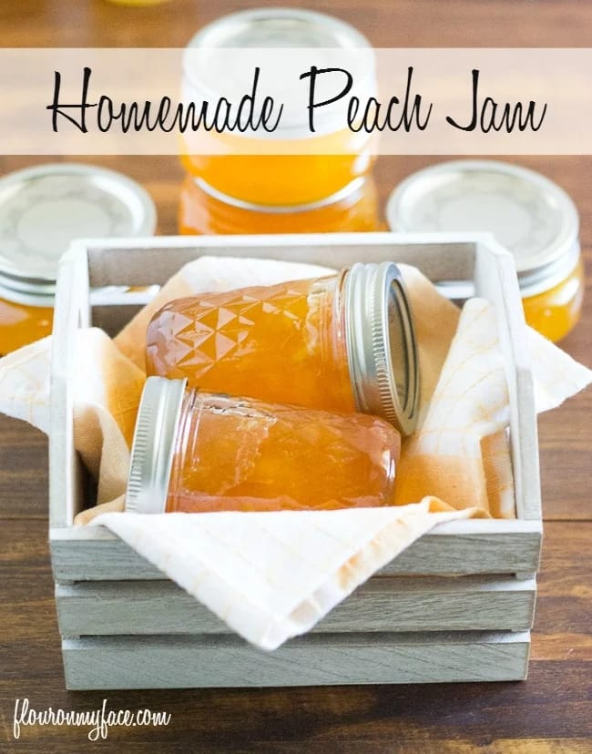 two glass jars of peach preserves laying inside a white wooden crate