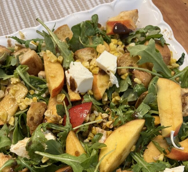 green leaf salad with peaches and corn on a white plate