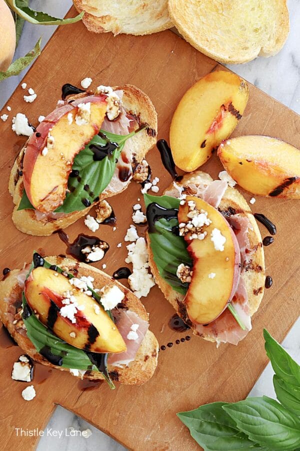 bread slices with grilled peaches, and basil sitting on a wooden cutting board