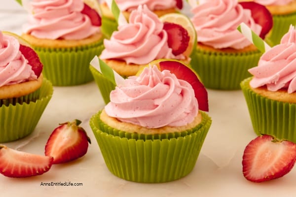 pink icing on a cupcake with green paper liner and cut strawberries sitting next to them