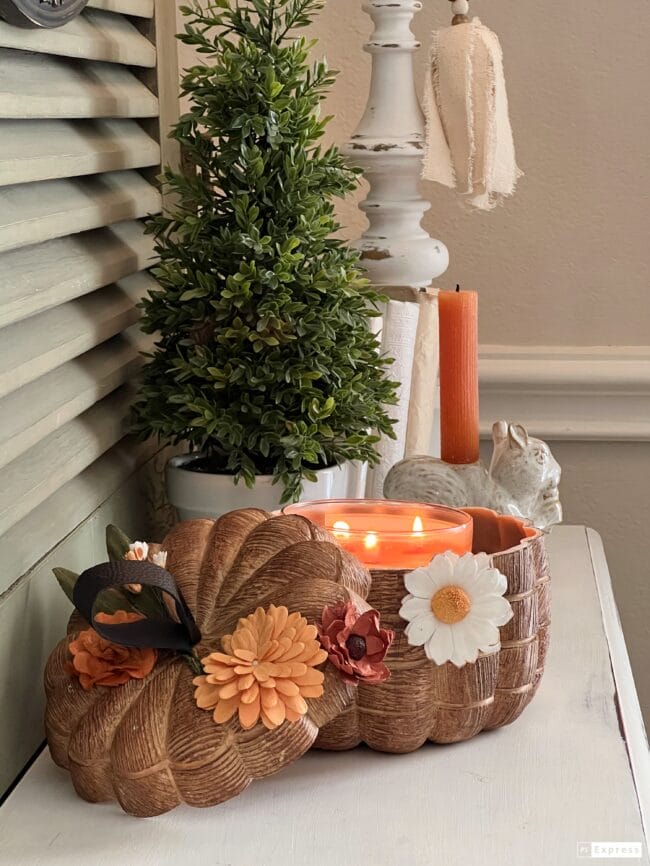 candle inside pumpkin bowl with topiary tree and squirrel candle in background