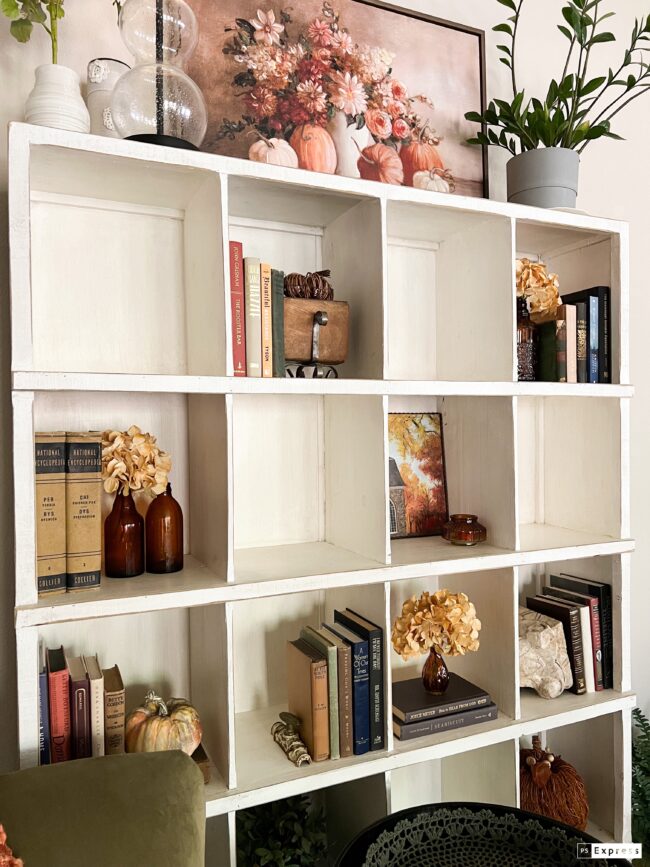 white cubby shelf with fall colored books, gold flowers and fall decor