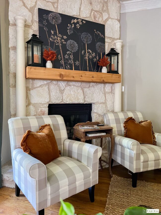 2 taupe checked chairs sitting in front of a mantel with a large black and gold dandelion print