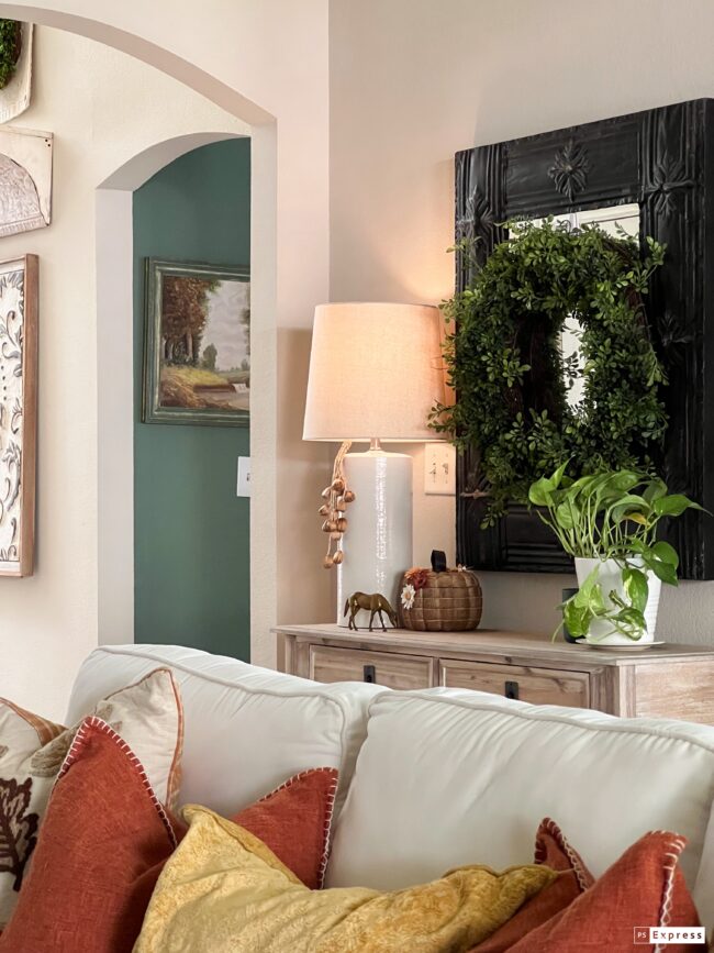 sofa table with a boxwood wreath hanging on a black mirror, lamp and plant