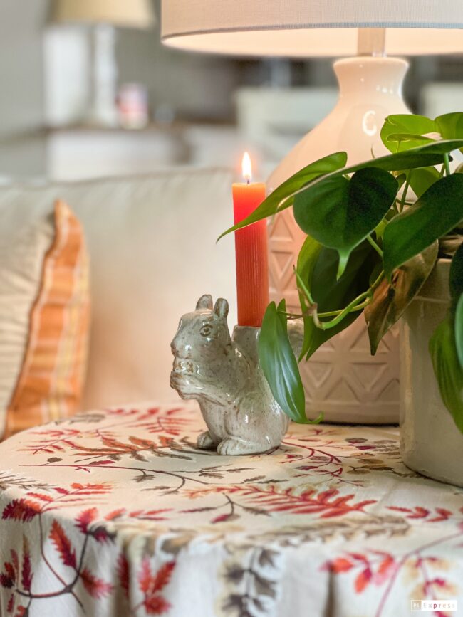 ceramic squirrel with orange candle on table with lamp and green plant