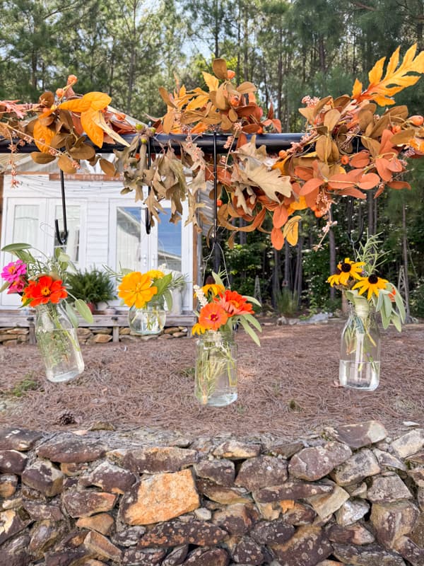 an outdoor table with a bar hanging over a table with leaves and bottles of fresh flowers 