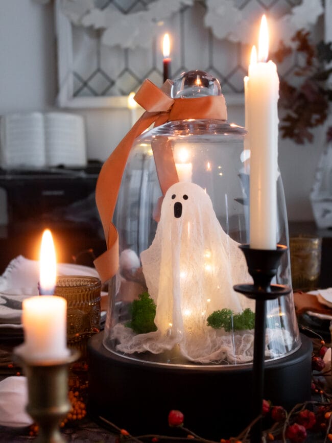 crafted ghost under a cloche with white candles