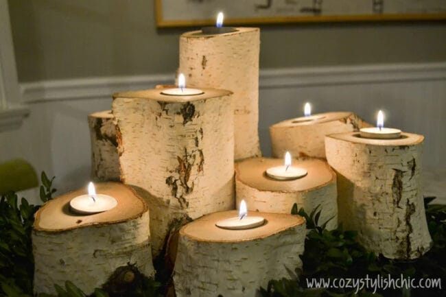 several white birchwood logs with tea lights and greenery as a centerpiece on table