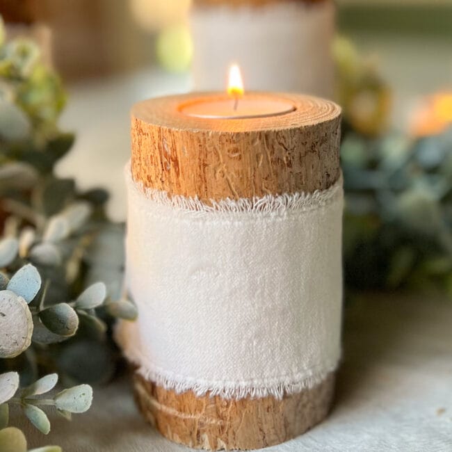 close up of a short tree branch with a tea light and white velvet ribbon tied around the middle.