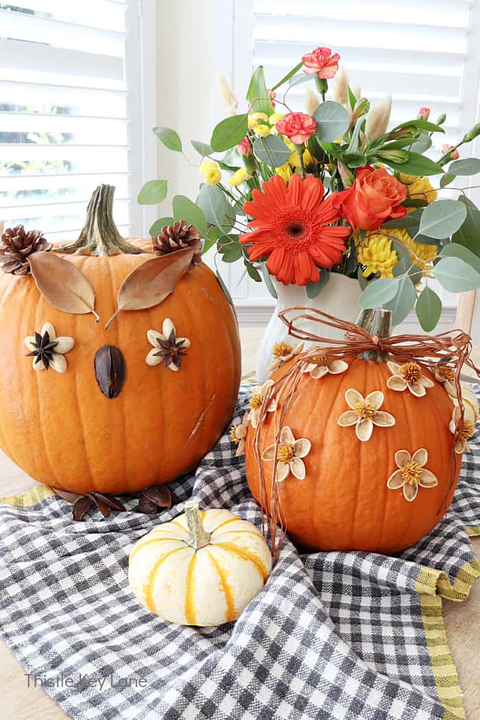 two orange pumpkins decorated for fall with flowers in vase on a table