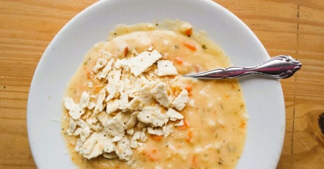 white bowl of soup with crunched up crackers and a spoon