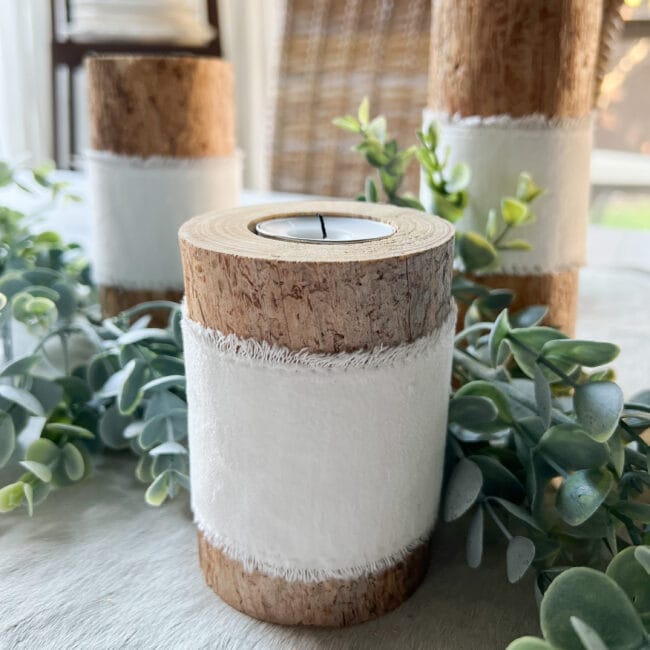 unlit rustic log candle holder with white ribbon around the middle