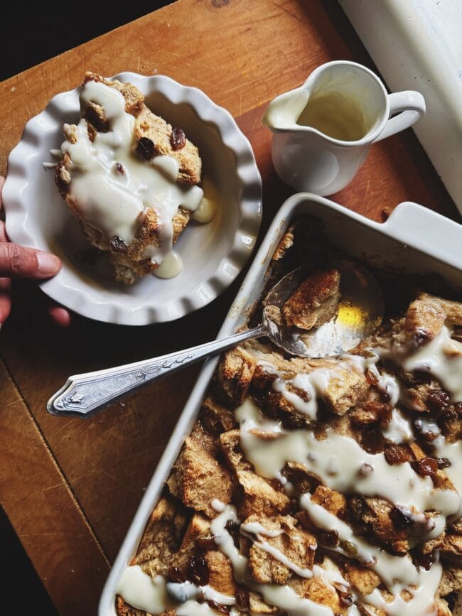 tray and white bowl with bread pudding inside and a large spoon and small white pitcher