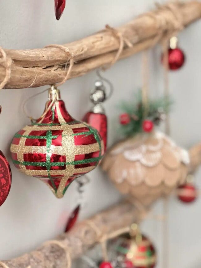 tree branch hanging on wall with red, green and natural Christmas ornaments on it