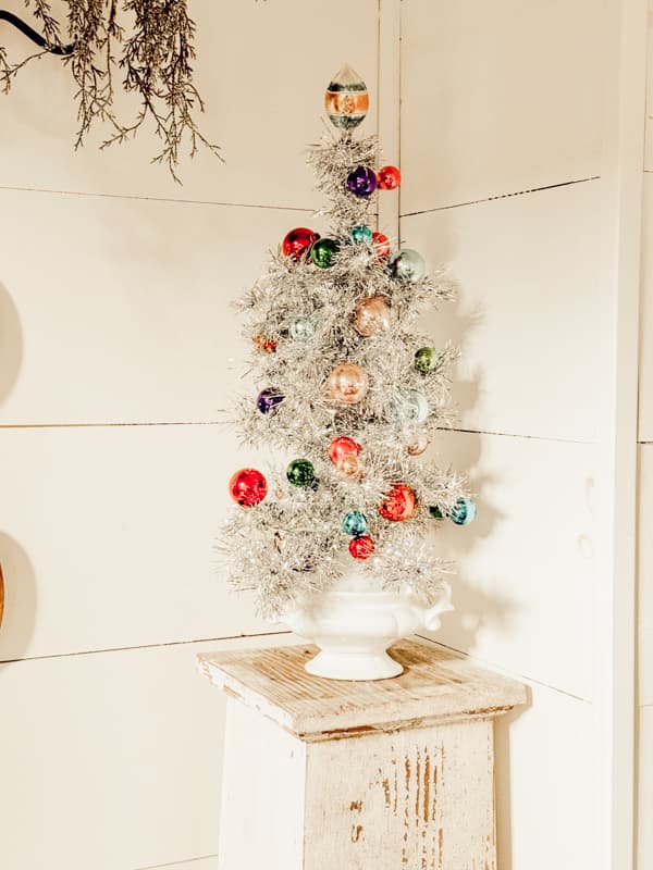 aluminum tree with multi colored Christmas balls on white stand in the corner