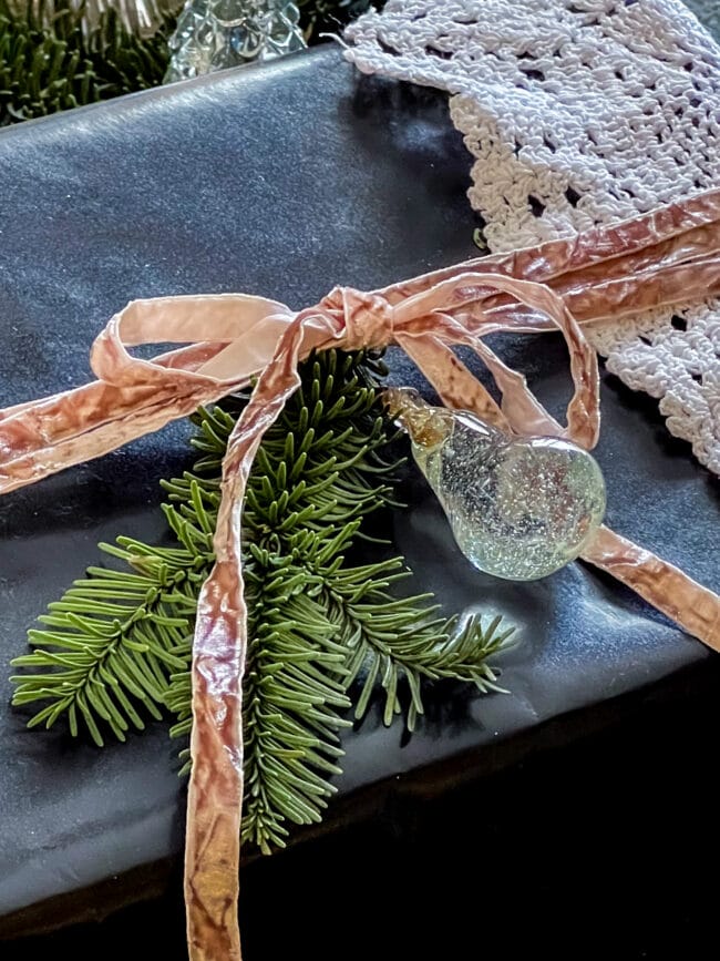 close up of black gift box with crushed velvet ribbon and a vintage doily and glass ornament