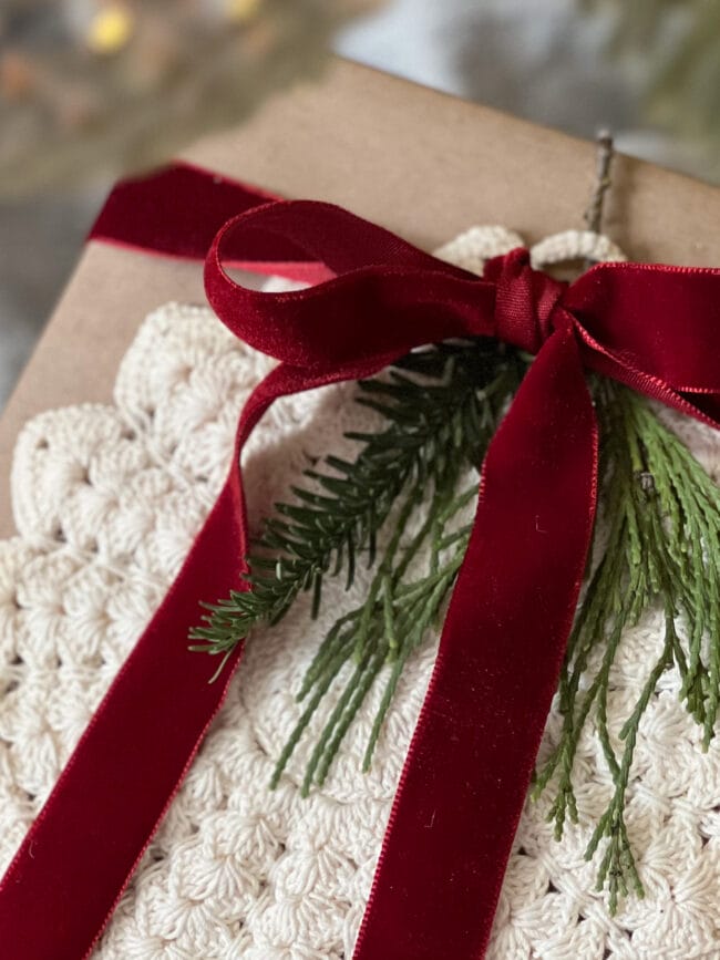 close up of brown gift with round doily, real greenery and deep red velvet ribbon