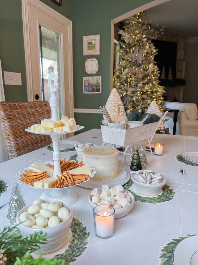 full table with white desserts and a 2 tiered tray with cheese and pretzels. A Christmas tree in background