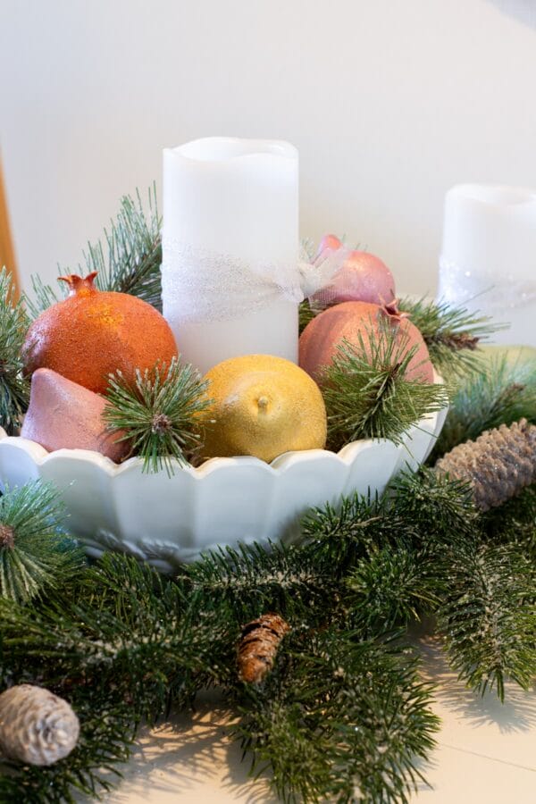 white bowls with greenery around the base and pastel fruit inside with a white candle