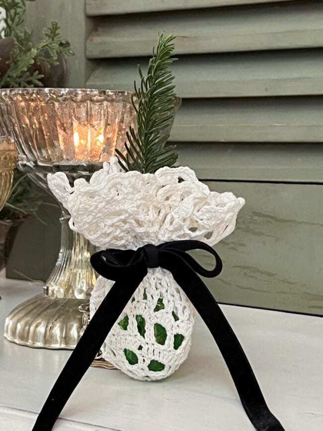 glass ornament wrapped in a vintage doily with black velvet ribbon and a piece of greenery coming through the top